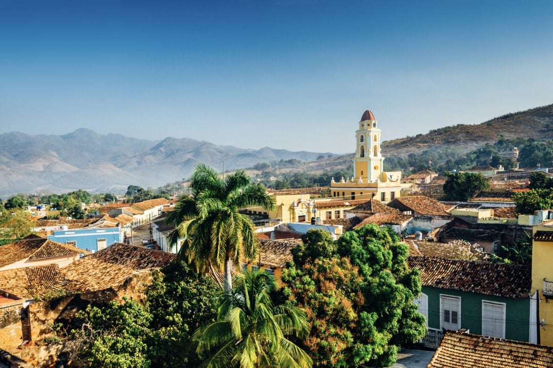 Panoramic view over the city of Trinidad, Cuba with mountains in the background and a blue sky. The bell tower belongs to the Iglesia y Convento de San Francisco.